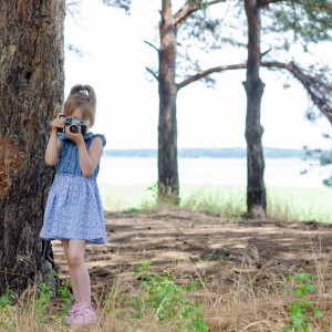 A little girl with a retro camera takes pictures in the forest, a copy of the free space. A small photographer, a rest and a hobby.